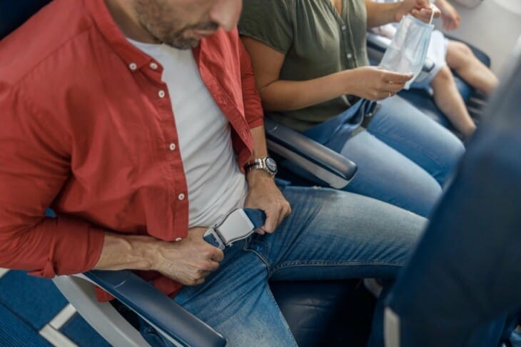 male passenger fastening seat belt on airplane