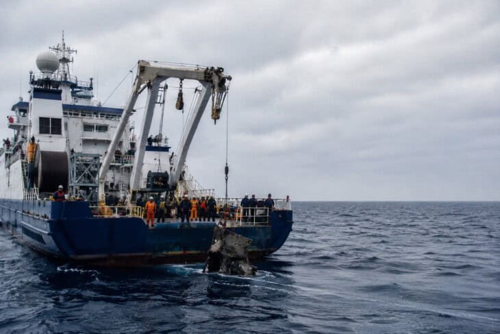 A recovery vessel on the open ocean, crew working on deck during a deep-sea search operation