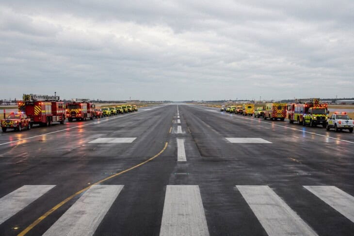 Airport runway lined with fire trucks and emergency vehicles positioned and waiting, ready for an aircraft emergency landing