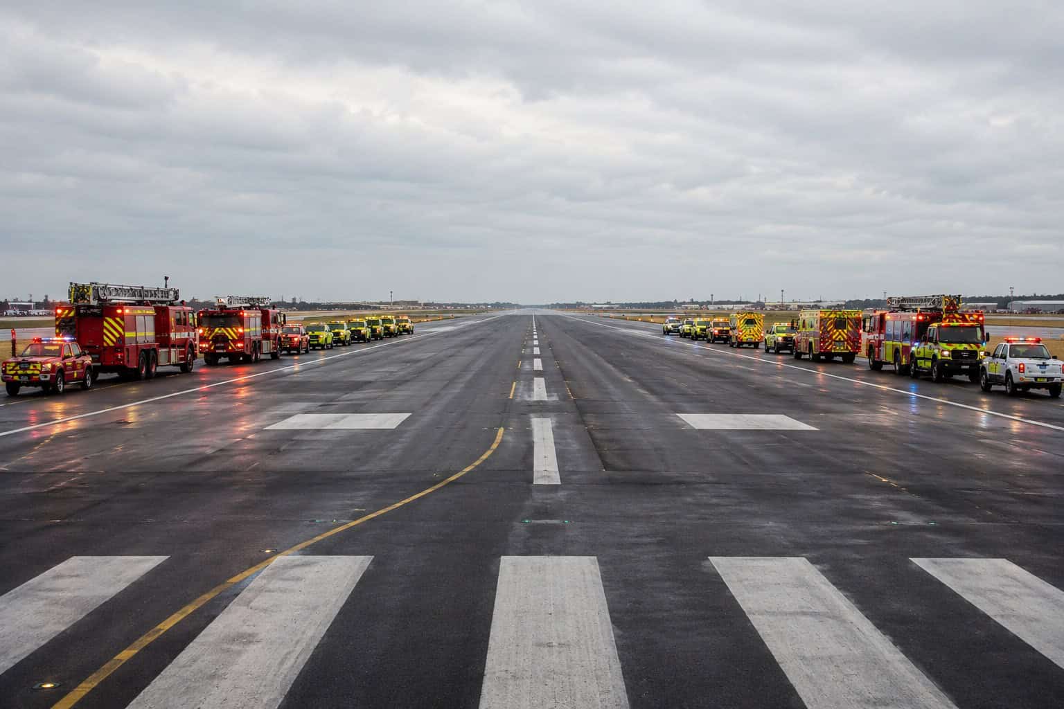 Airport runway lined with fire trucks and emergency vehicles positioned and waiting, ready for an aircraft emergency landing