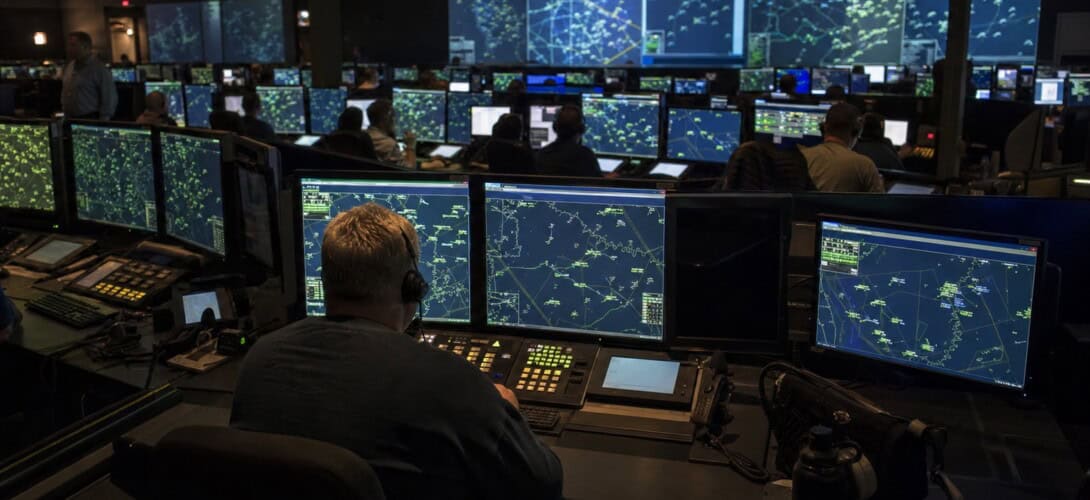 Air Route Traffic Control Center with controllers at radar workstations in a dimly lit operations room