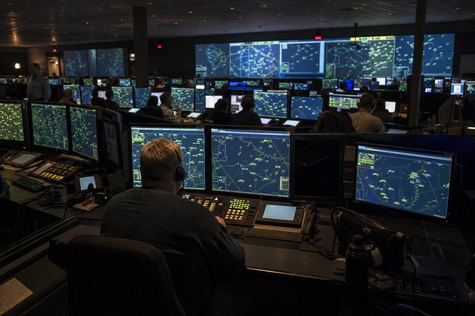 Air Route Traffic Control Center with controllers at radar workstations in a dimly lit operations room