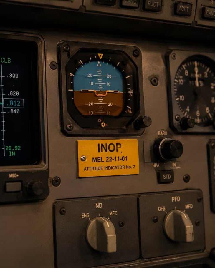 Close-up of an aircraft cockpit instrument panel with an orange INOP placard affixed to one of the controls, indicating an inoperative item deferred under the MEL