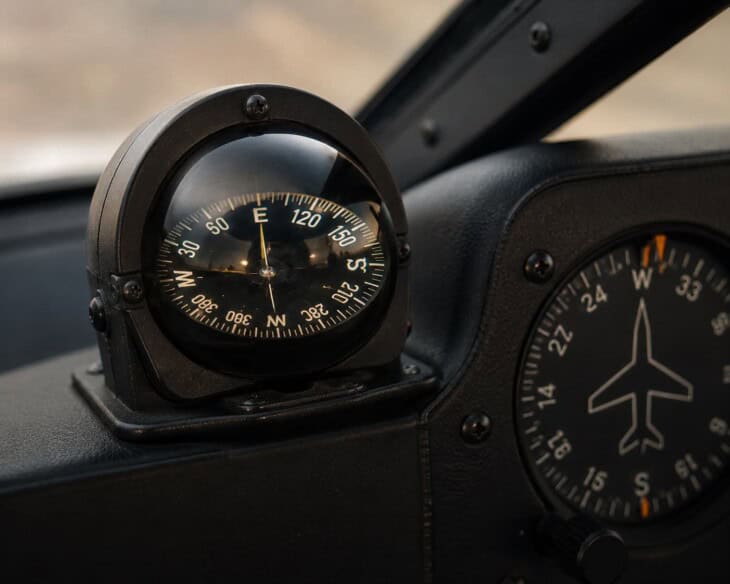 Magnetic compass mounted in an aircraft cockpit, liquid-filled bowl type, showing degree markings and cardinal directions, with instrument panel partially visible