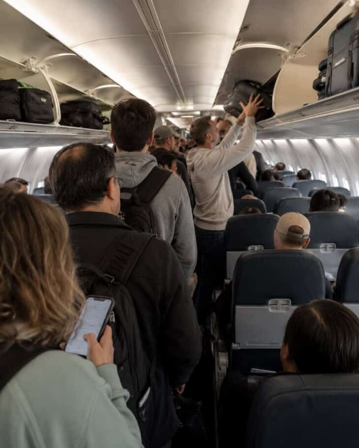 Passengers crowded in a narrow aircraft aisle waiting while overhead bins are loaded