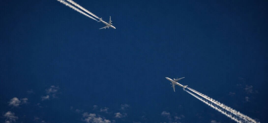 Two commercial aircraft at high cruising altitude with contrails, showing the relative proximity that TCAS is designed to prevent becoming a collision