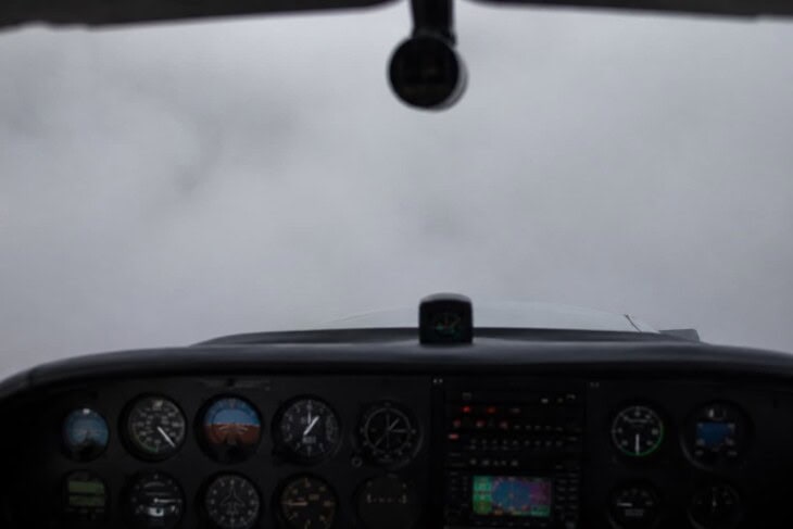View from inside a light aircraft cockpit flying through thick cloud with no visible horizon, instrument panel visible below