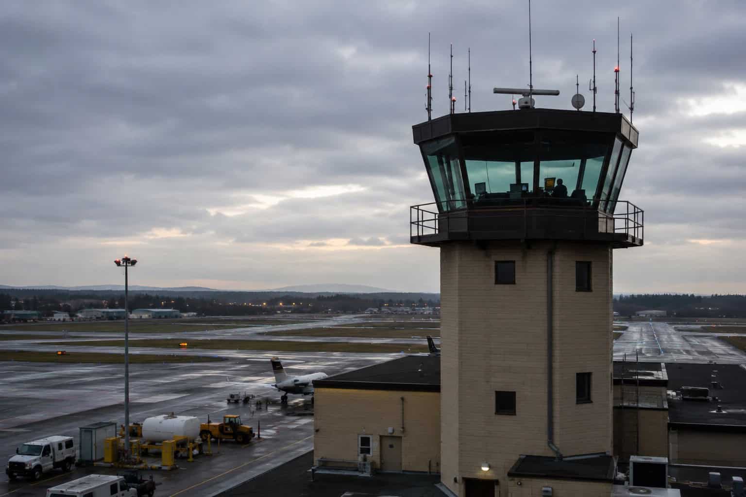 The control tower of a regional airport photographed from outside in late afternoon light, the runway visible below