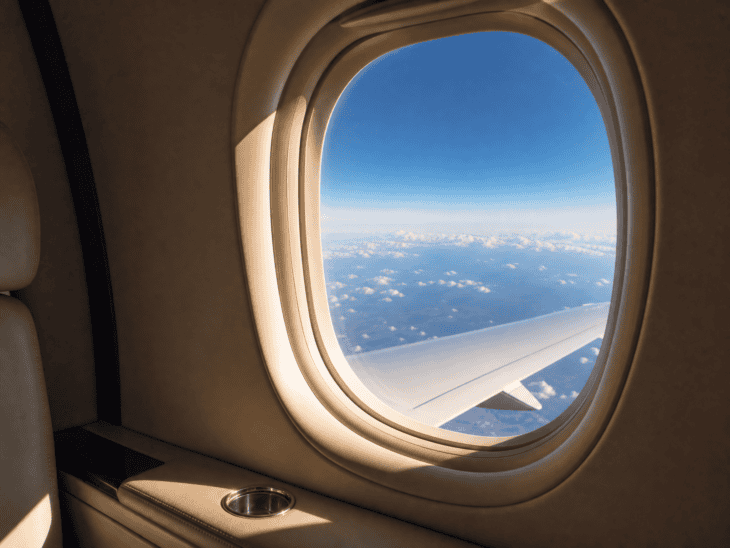 View through a private jet window in flight, blue sky and scattered clouds visible below