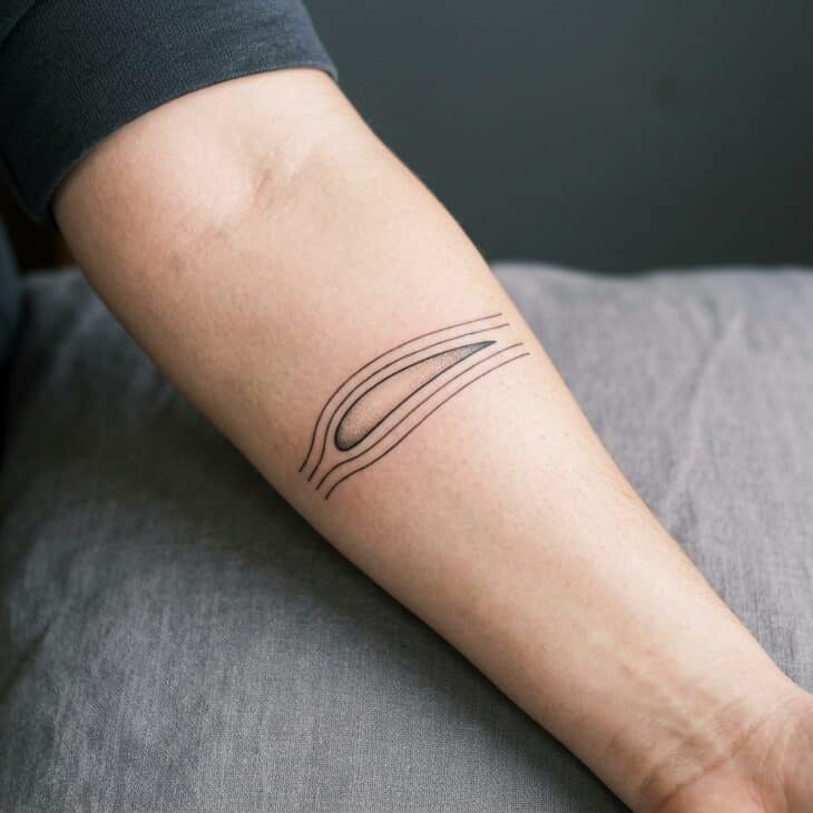 Fine-line airfoil tattoo on an adult forearm with smooth airflow lines above and below the wing shape