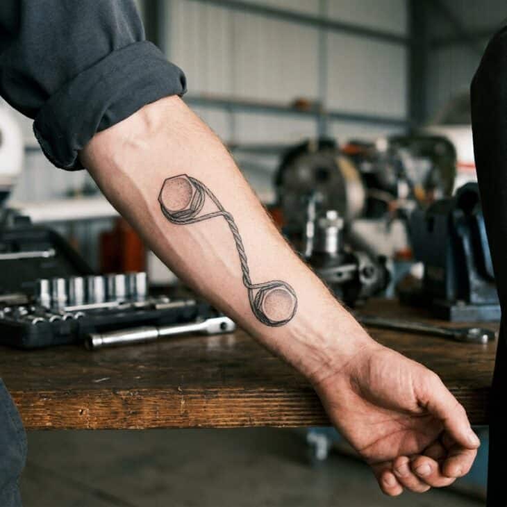 Subtle aviation mechanic tattoo on an adult forearm showing twisted safety wire wrapped around two small bolt heads