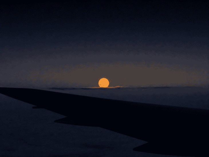 A full moon rising above a dark aircraft wing at cruise altitude, the moon warm orange-yellow in its low position, the wing a dark silhouette against a deep twilight gradient sky
