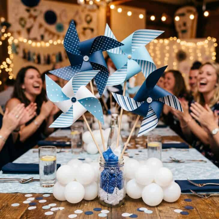 Party table centerpieces with oversized paper pinwheels in navy, sky blue, and white on wooden dowels in mason jar bases