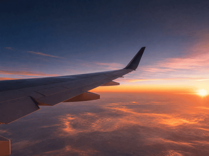 Aircraft wing glowing amber in the light of a setting sun, thin clouds far below, twilight blue sky above