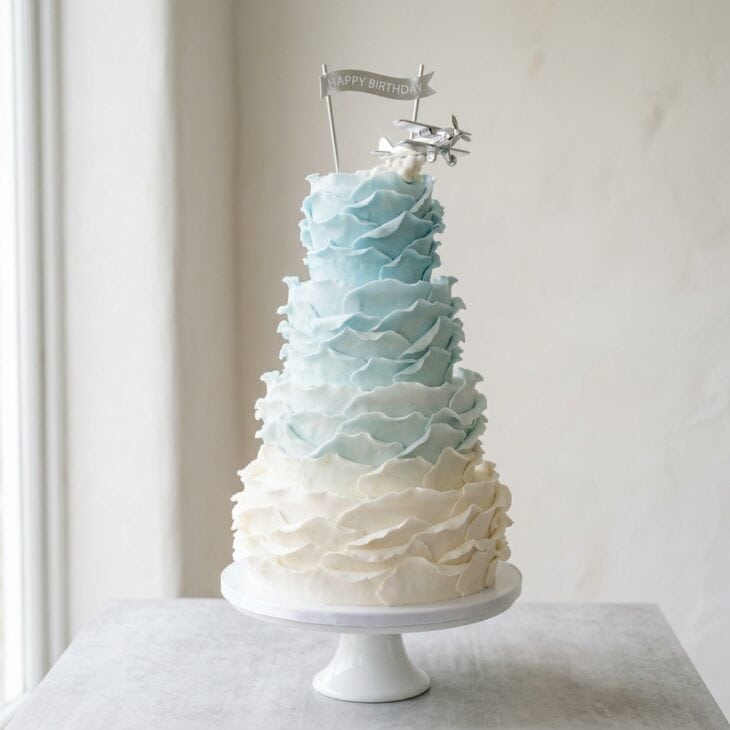 White to blue ombre ruffle cake resembling clouds with a small silver plane on top