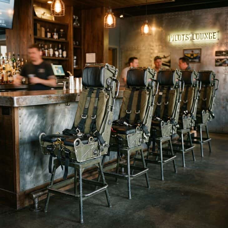Bar stools styled like fighter jet ejection seats at a metal counter