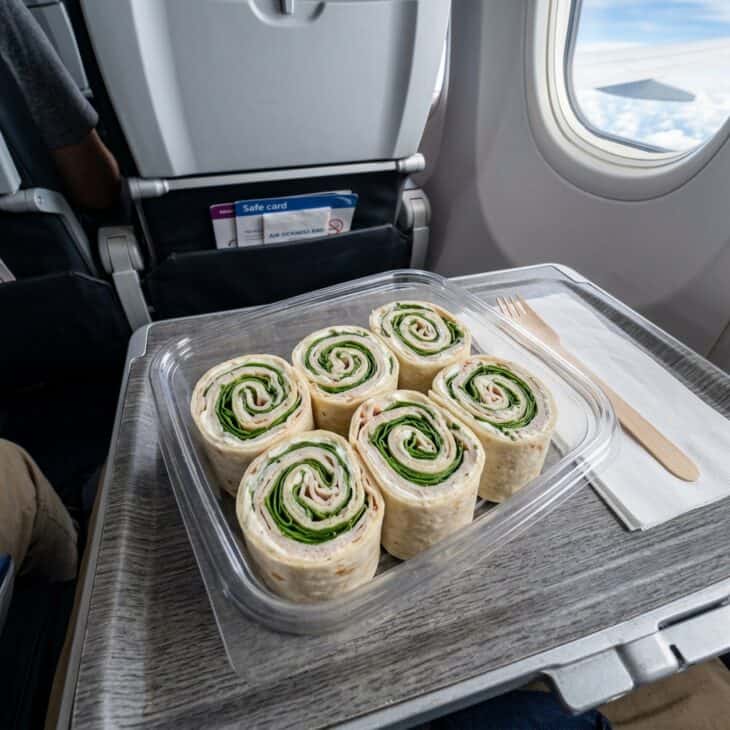 Pinwheel sandwich spirals with turkey and spinach in a clear container on an airplane tray table