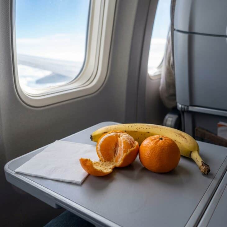 Two mandarin oranges and a banana on an airplane tray table beside a napkin