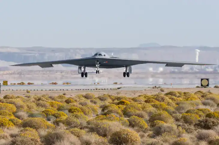 A Northrop Grumman B-21 Raider test aircraft flying low over desert scrub with its landing gear down