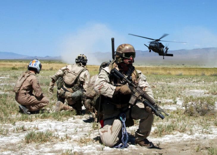 Pararescuemen and a simulated survivor watch as an HH 60G Pave Hawk helicopter comes in for a landing