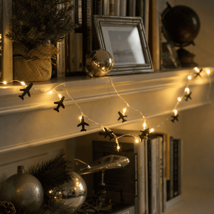 Airplane silhouette charms punctuate a warm white light strand along a living room shelf.