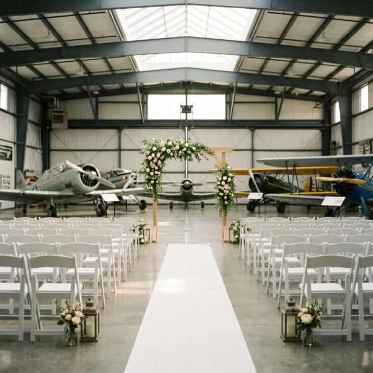 A ceremony aisle is set beneath restored aircraft inside a museum exhibit hall.