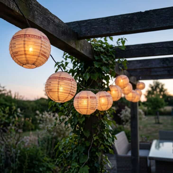 Boarding-pass lantern lights glow warmly along the pergola beam at dusk.
