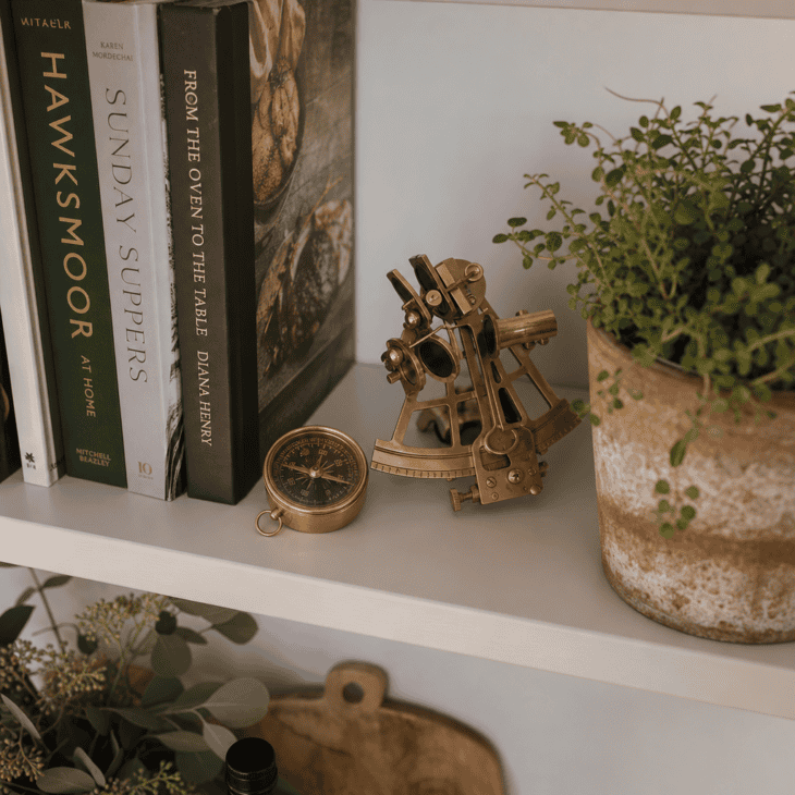 A brass compass and sextant dress the open shelf beside the cookbooks.