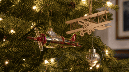 Christmas tree branch strung with lights holding a glass propeller plane ornament, a wooden biplane silhouette ornament, and a mercury glass ornament