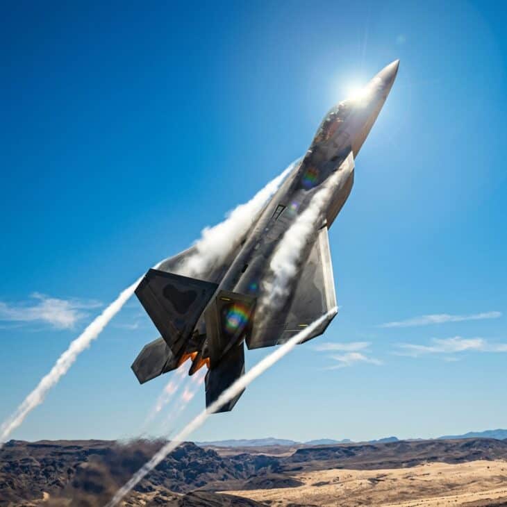 Fighter jet climbing steeply into a clear desert sky with wingtip vapor