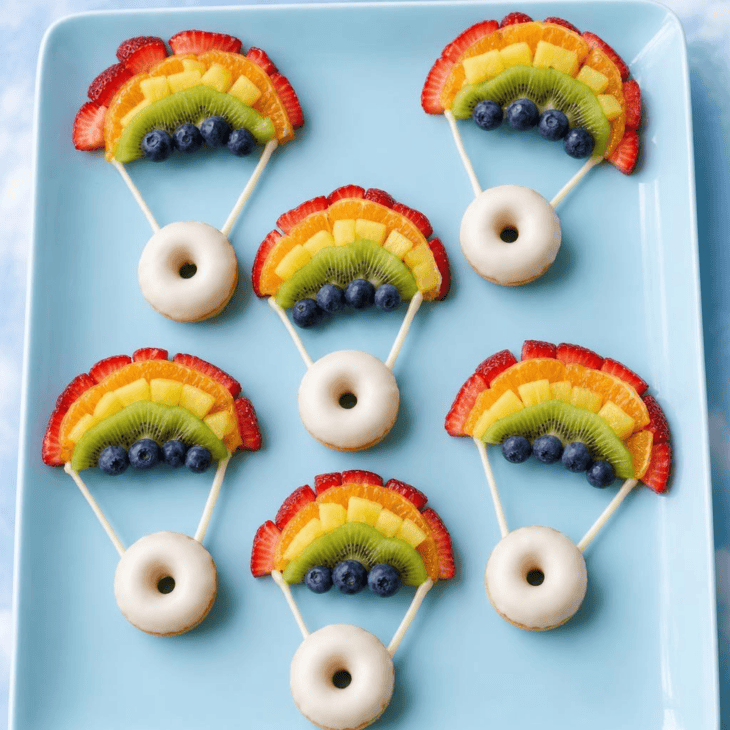 A fruit arc and two chocolate lines turn a mini donut into a parachute.