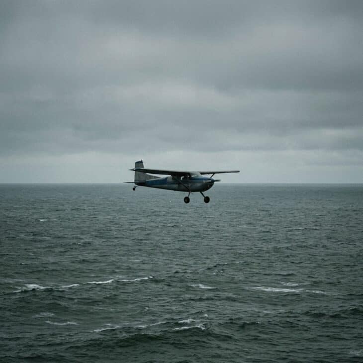 Lone single-engine monoplane flying over open ocean under an overcast sky