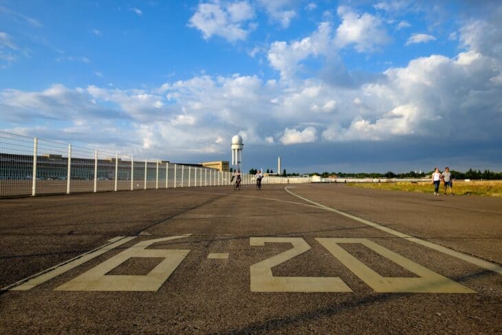 People walking on a former runway at Tempelhofer Feld, with the terminal and radar tower behind