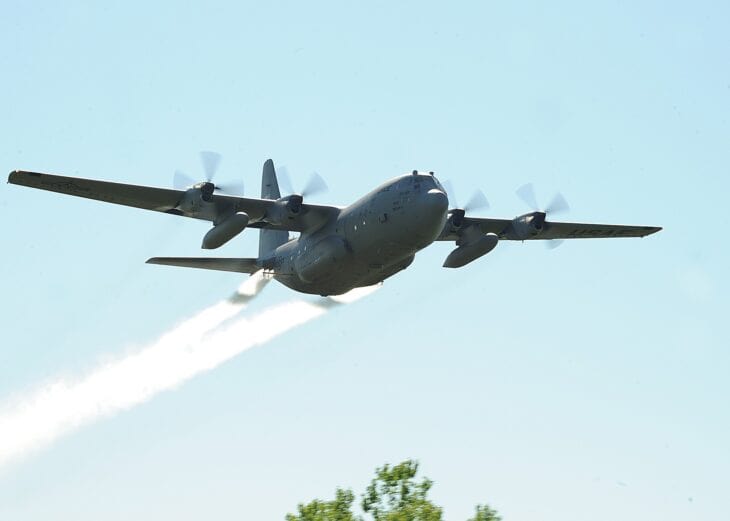Air Force Reserve C-130 Hercules of the 910th Airlift Wing flying low over trees with two white spray plumes trailing from its tail