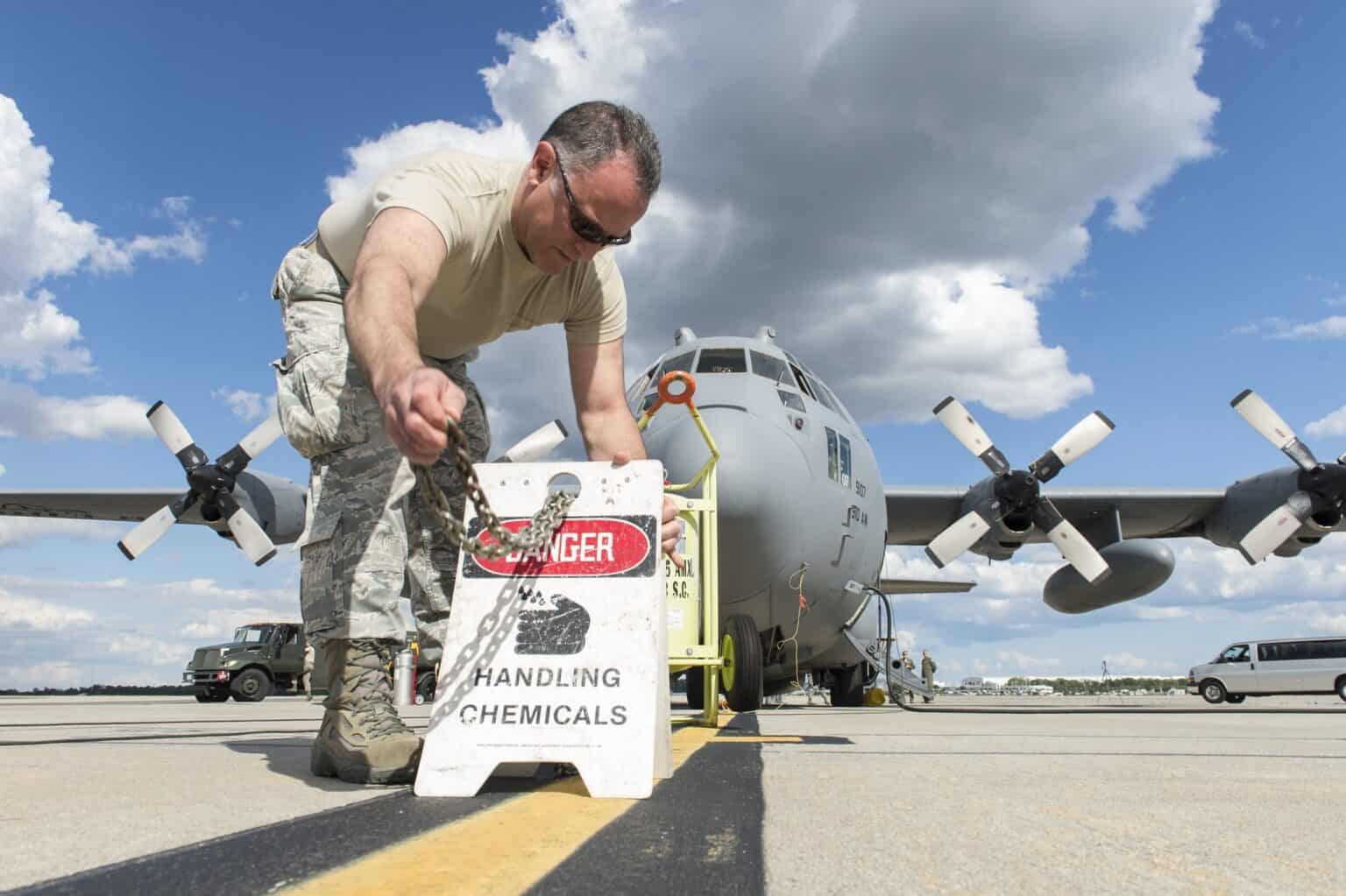 An airman posts warning signs on the ground around a parked C-130 Hercules before insecticide loading begins