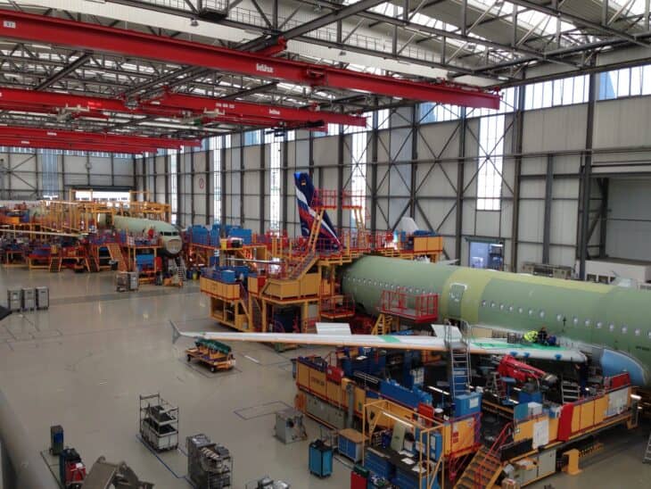Green-primed Airbus A320-family fuselages in work platforms on final assembly line 3 at Airbus in Hamburg, with a wing section on a cradle in the foreground
