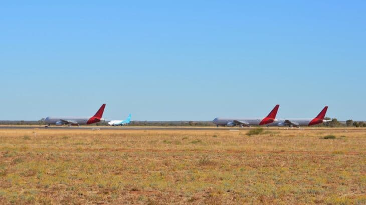 Stored Boeing 767s with red Qantas tails and a Boeing 737 parked on the dry grassland at Alice Springs Airport
