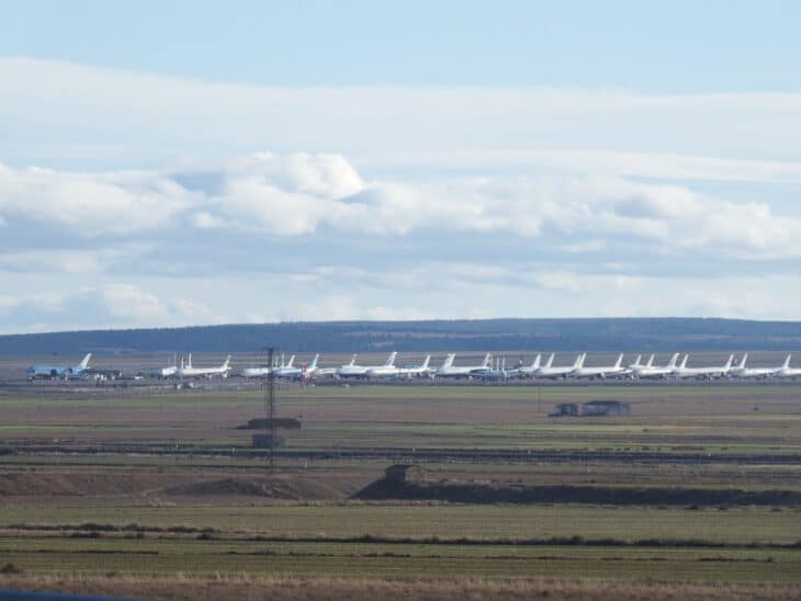 A long line of parked airliners on the Teruel Airport apron, seen across flat farmland under a cloudy sky