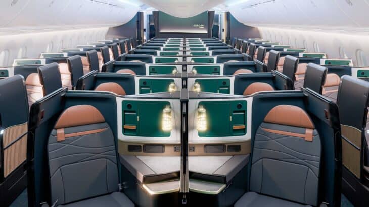 Rendering of an Alaska Airlines 787 Aurora Suites cabin, looking aft over rows of suites with copper headrests and green storage consoles