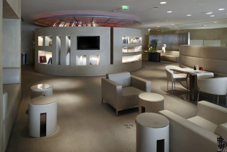 Pale armchairs and a curved display wall in the Air France La Première lounge at Paris Charles de Gaulle Terminal 2E
