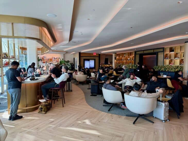 Travelers in armchairs around a curved bar in the Chase Sapphire Lounge at JFK Terminal 4