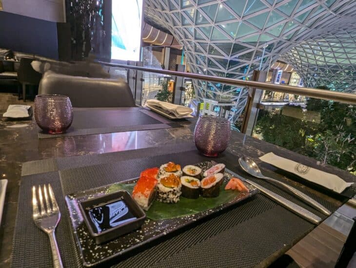 A sushi plate on a dining table in Qatar Airways' Al Mourjan The Garden lounge, with the lattice roof of The Orchard behind