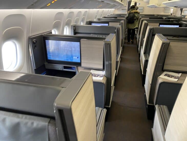 Rows of ANA The Room business class suites with large seatback screens and sliding doors in a Boeing 777-300ER cabin