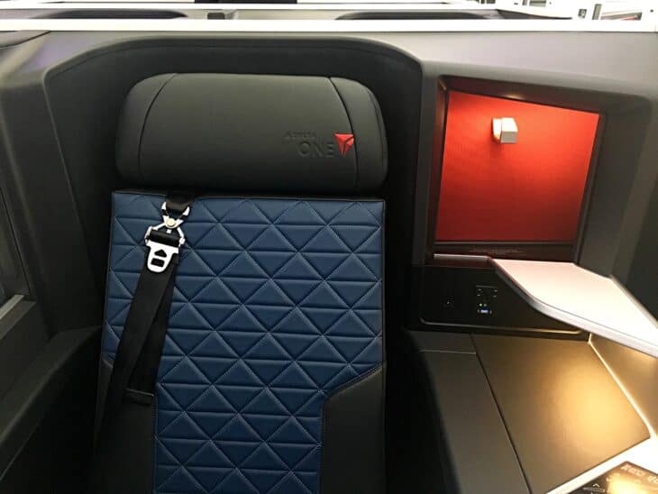 A Delta One Suite on an Airbus A350-900 with a navy quilted seat back, red-lit side panel and suite door