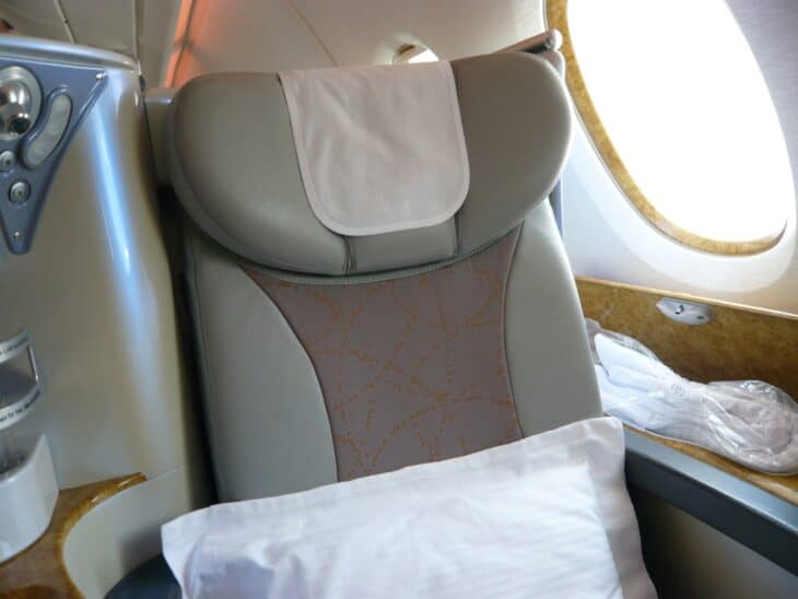 An Emirates business class seat with a pillow and a wood-trimmed side console beside the window on an Airbus A380