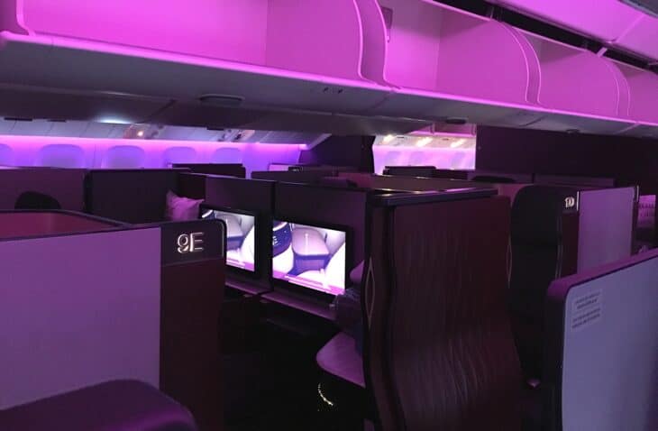 Qatar Airways Qsuite business class suites with privacy doors under purple mood lighting on a Boeing 777-300ER