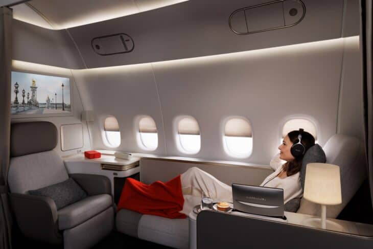 Passenger reclining on the chaise longue of the new Air France La Première suite, with five windows, a floor lamp and the seat beside her