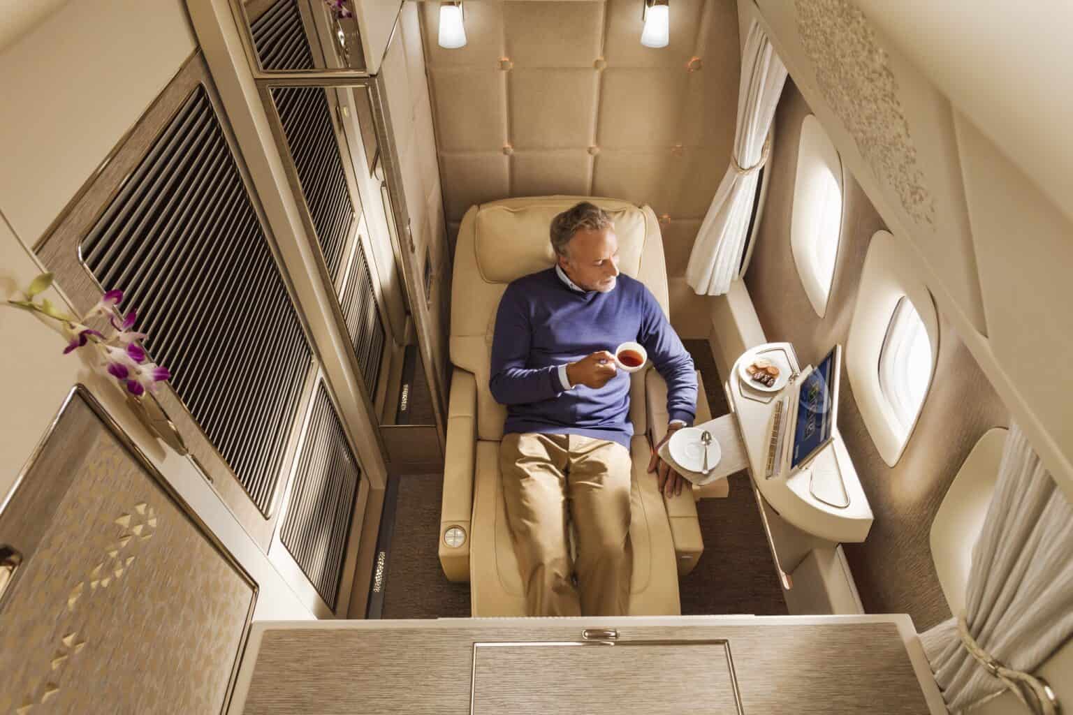 Overhead view of a passenger with a cup of tea in the Emirates Boeing 777 first class private suite, the seat reclined and the sliding doors on either side