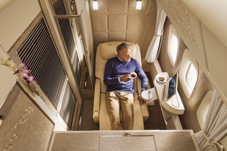 Overhead view of a passenger with a cup of tea in the Emirates Boeing 777 first class private suite, the seat reclined and the sliding doors on either side