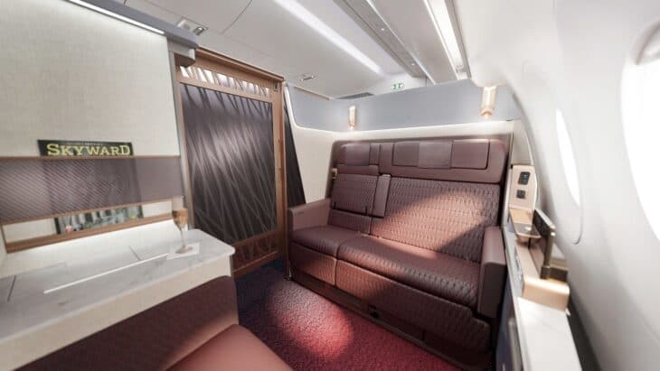 Japan Airlines A350-1000 first class suite with a wide burgundy leather couch, a sliding door and a marble side table with a glass of champagne